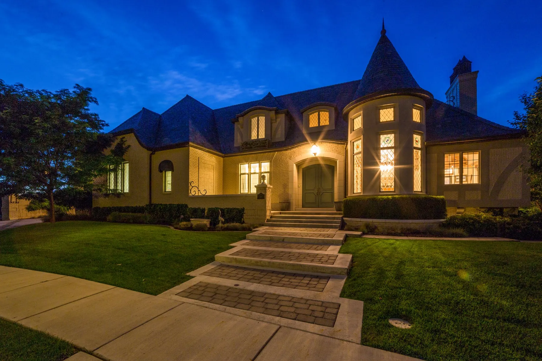 A home lit at blue hour with warm uplighting on the façade and landscaping